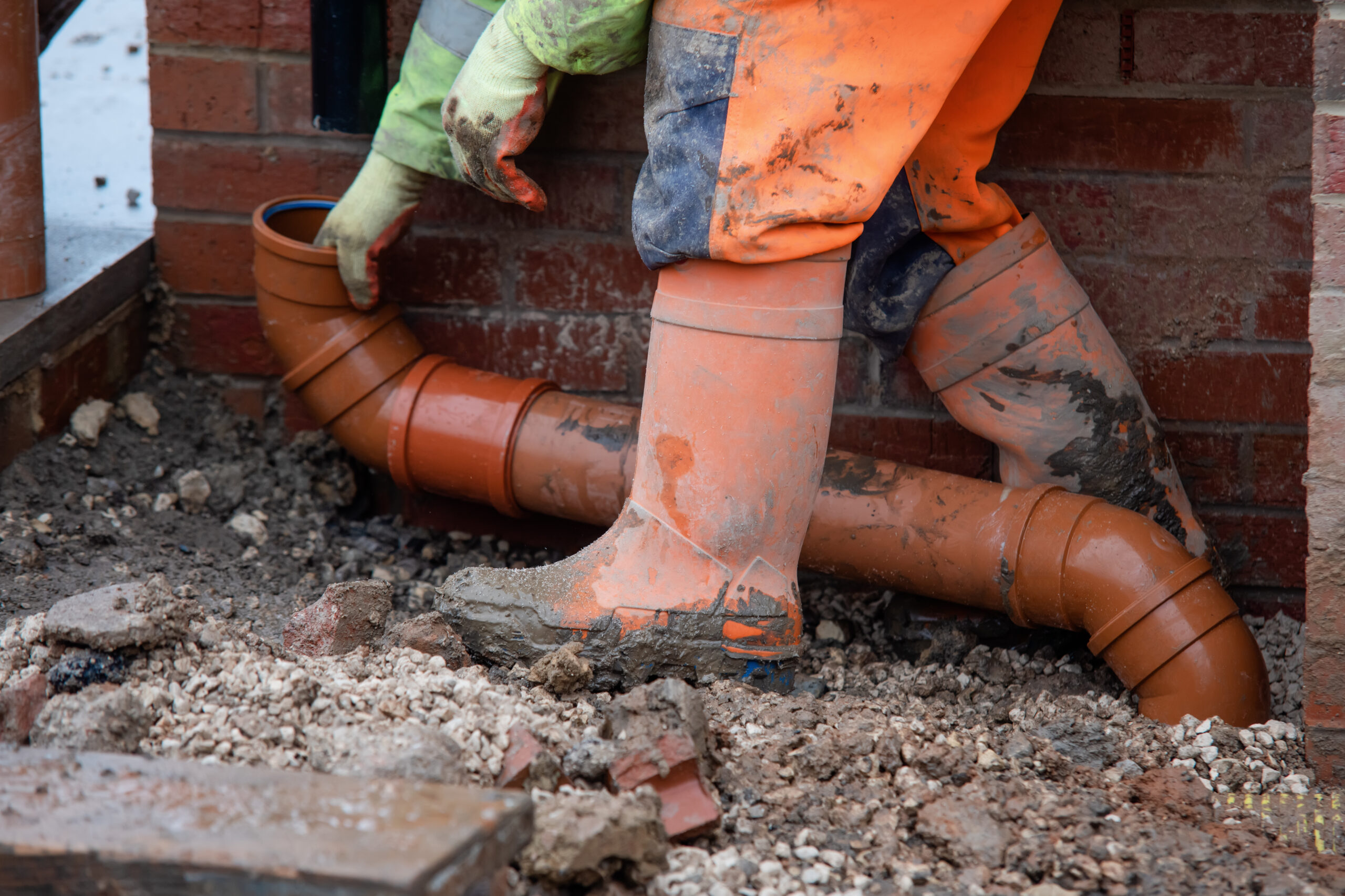 Groundworker fitting plastic drainage pipe to connect down pipe from the roof of new build house to the underground drainage network